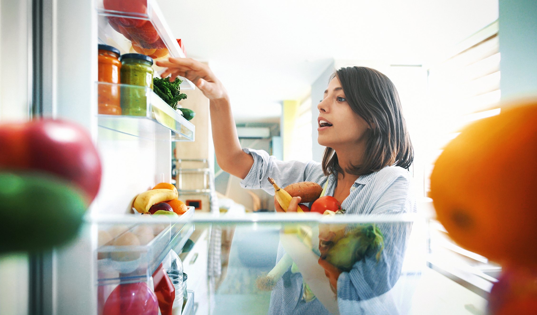 Eine junge Frau, die frische Lebensmittel in einen Kühlschrank räumt